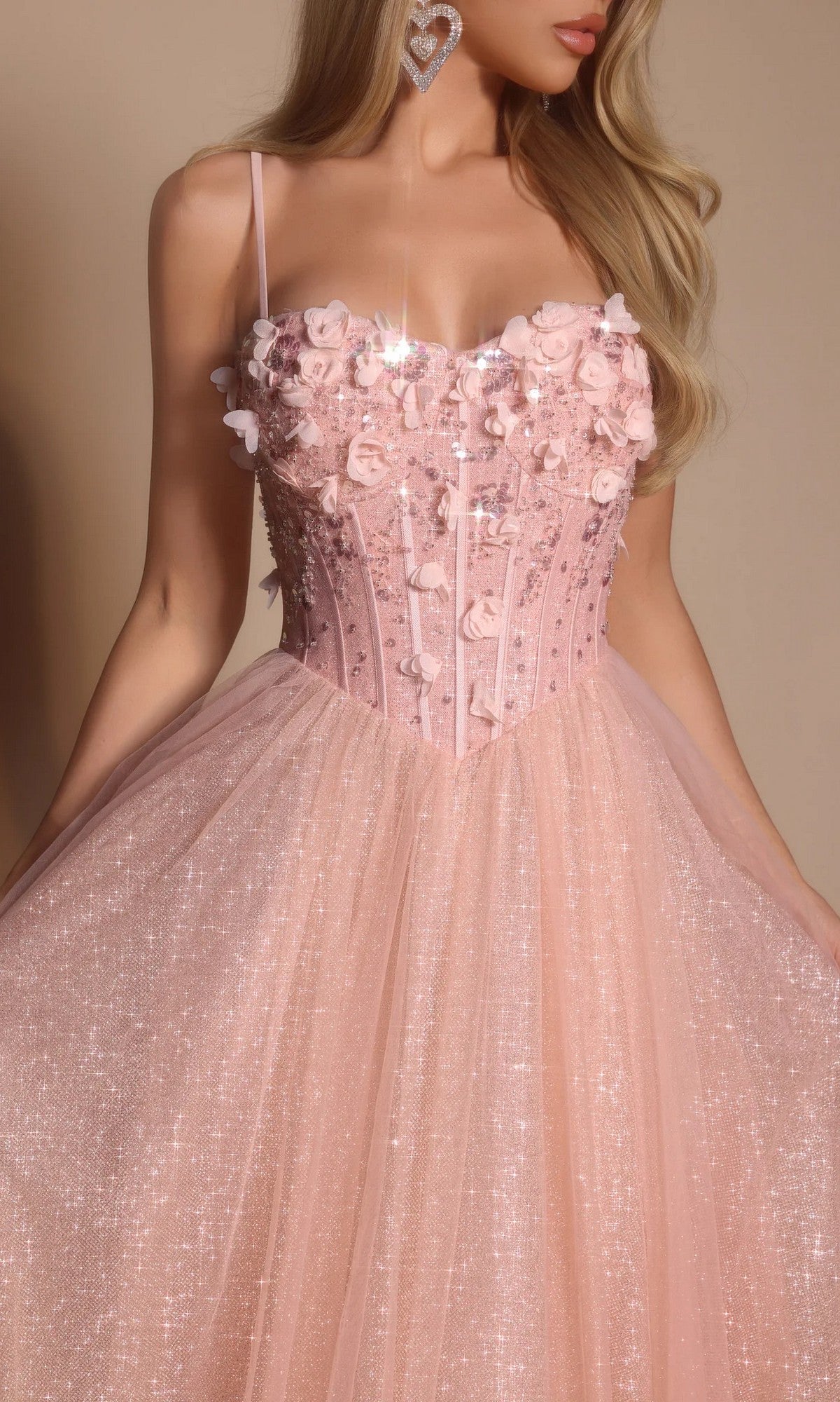 A woman wears the Portia and Scarlett PS26146 Glitter Prom Ball Gown, a pink tulle dress with a boned corset bodice, thin straps, and 3D floral appliqués.